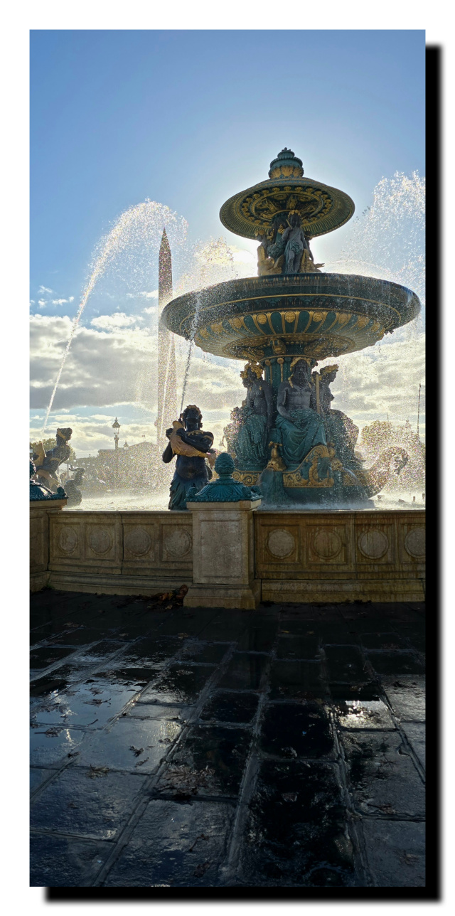Les pavés du trottoir mouillés, derrière une fontaine avec de l'eau qui jaillissait. En dernier plan, l'obélisque, et le ciel bleu.