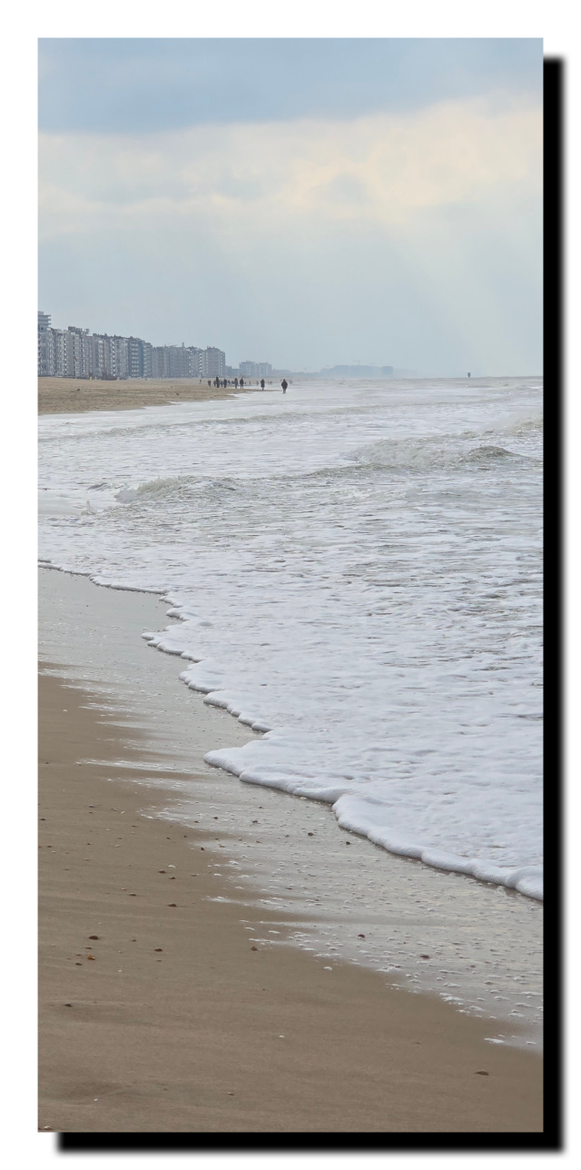Une longue plage avec des immeubles au fond.  À gauche, au fond à droite il y a les bras du soleil