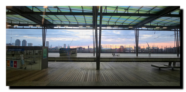 Au premier plan la gare d'Ostende avec son plafond bleu, vert. Au fond le haut d'un bateau, on aperçoit les couleurs orangées du jour qui se lève.