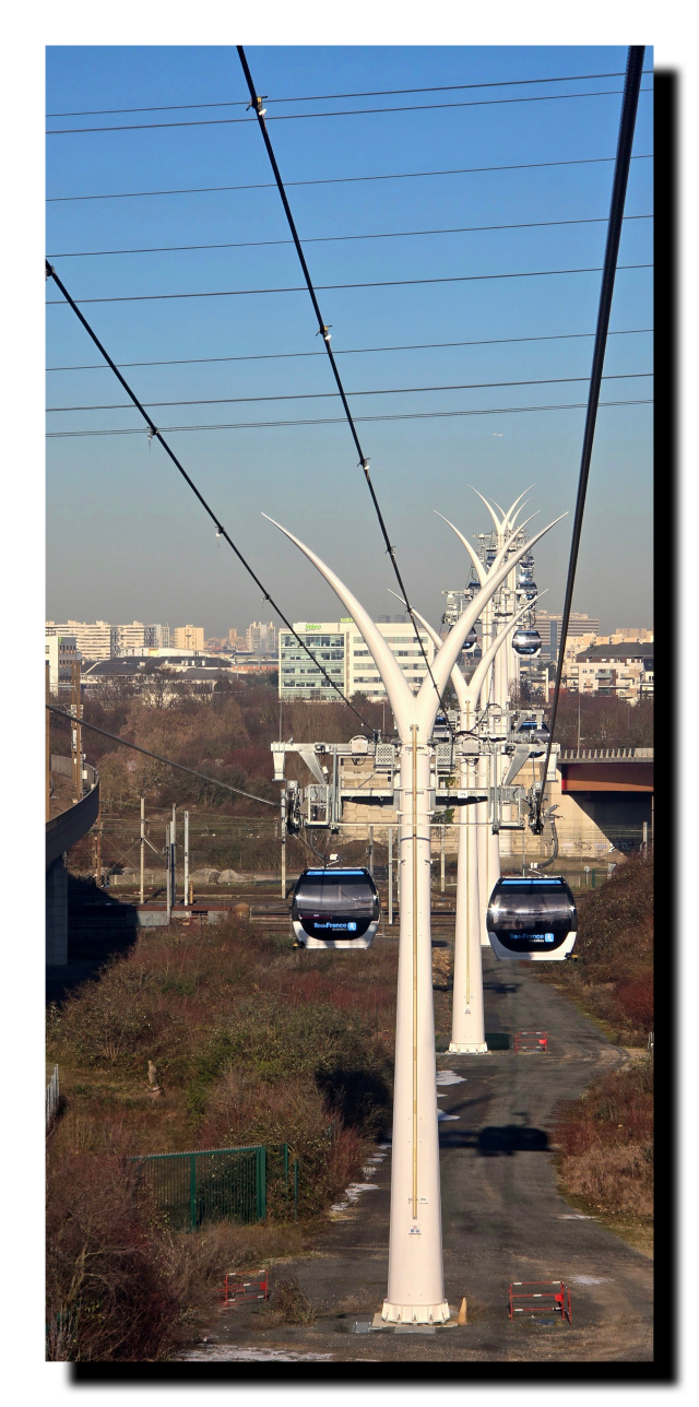 Alignement de pylônes de téléphériques au milieu une cabine de chaque côté. Le ciel est cadrillé par les cables du téléphérique.