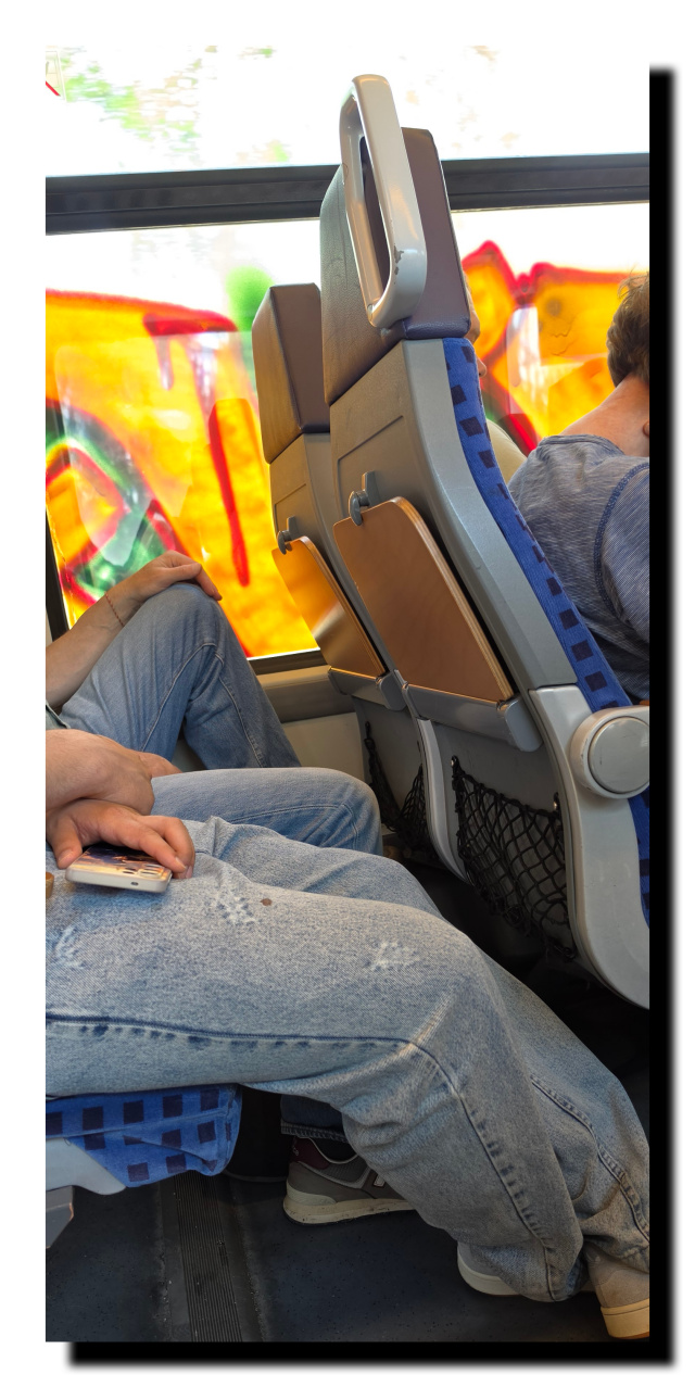 Des gens assis dans un train avec les vitres recouvertes de graffitis.
