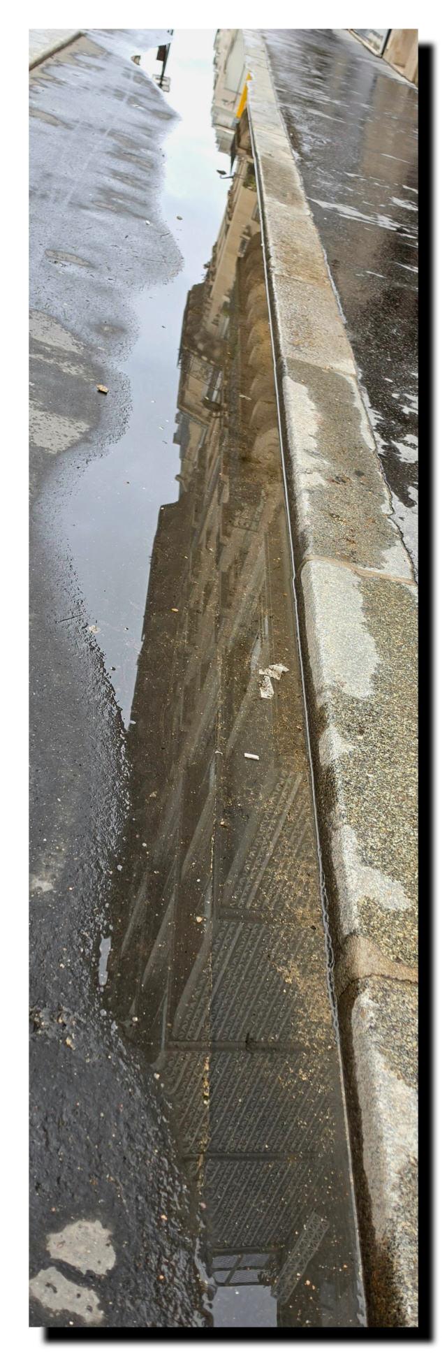 Façade d'un imleuble qui se reflète dans une flaque d'eau prés d'eau d'un trottoir.