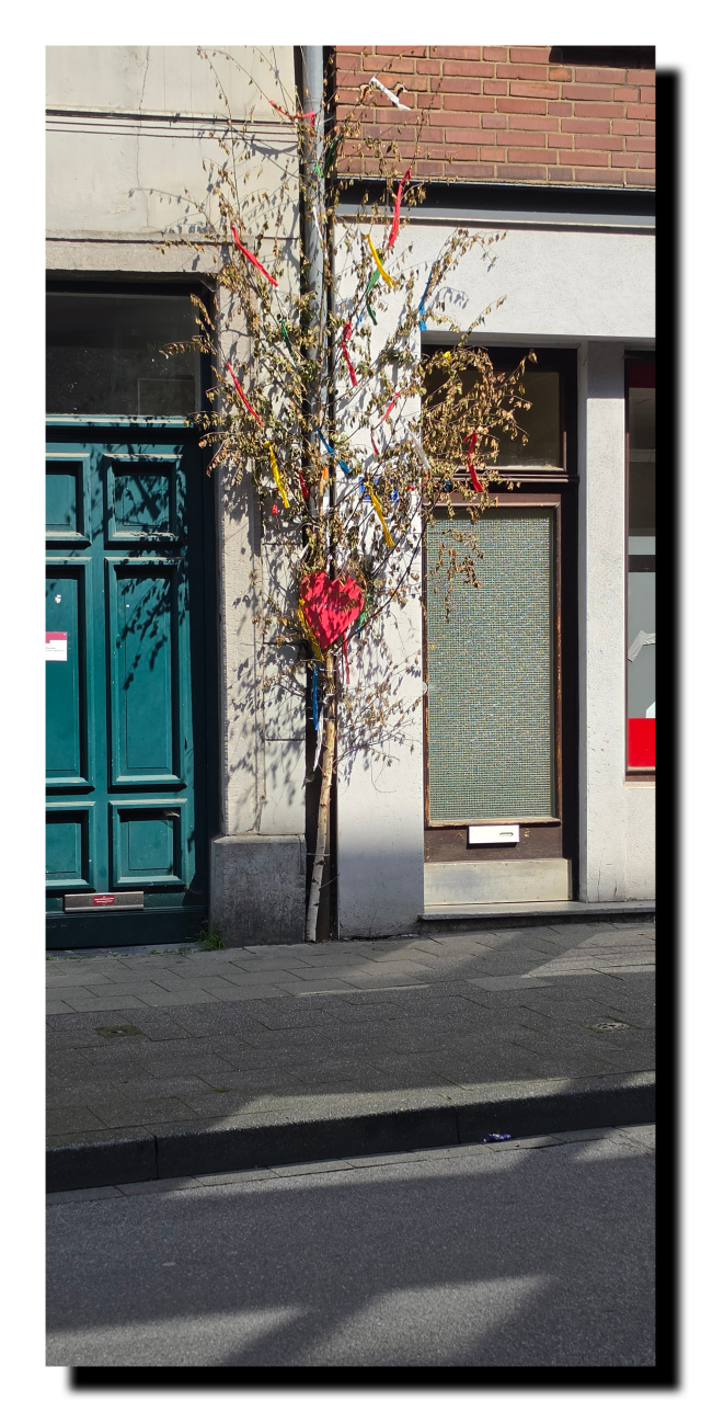 Une branche de bouleau, entre 2 portes, décorée avec des bouts de tissus, et d'un cœur rouge. Cela a un rapport avec le premier mai.