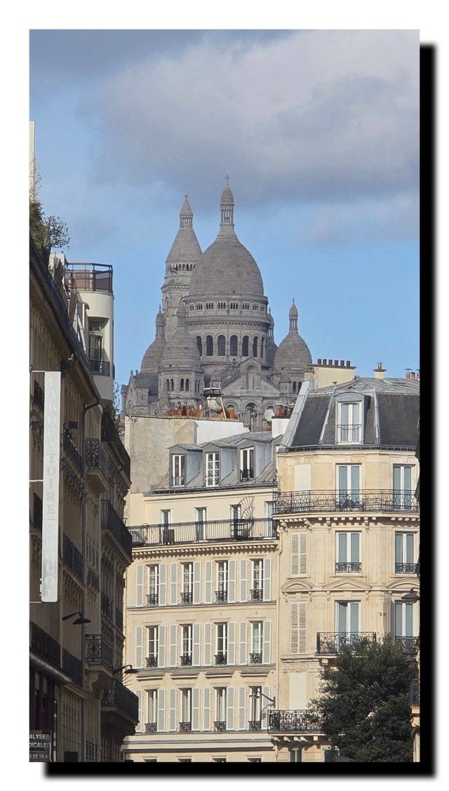 Au premier plan un immeuble, au fond Montmartre avec un nuage gris au dessus.