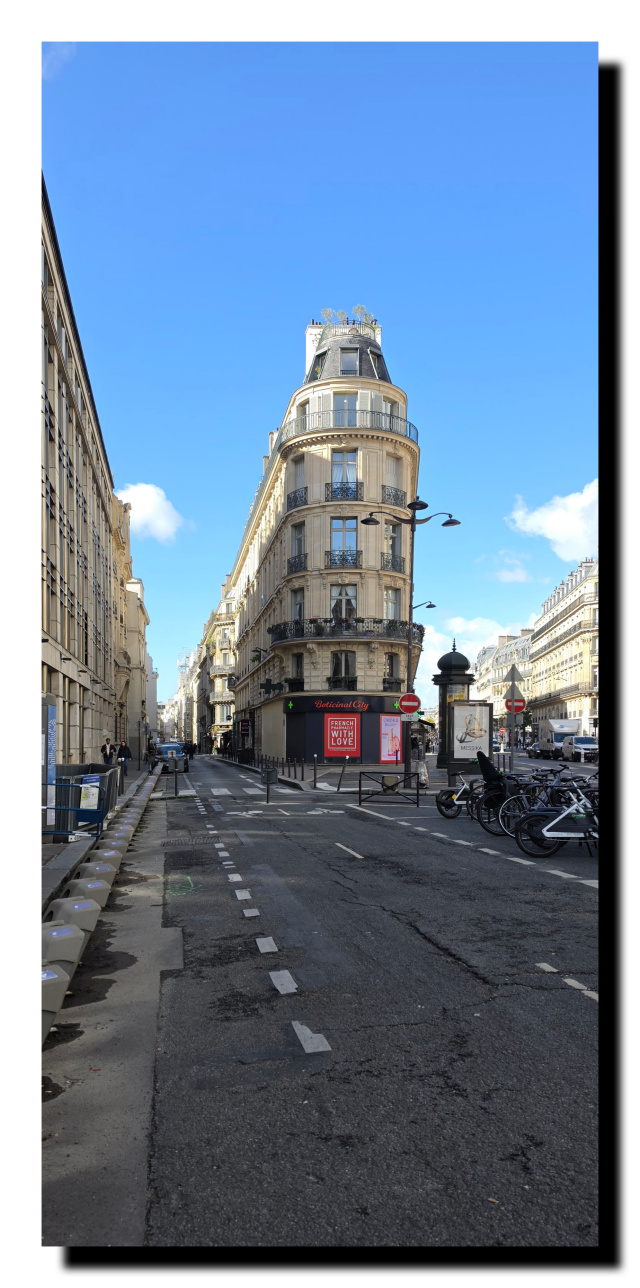 Rue avec du marquage au sol, à gauche la façade d'un immeuble, en face un immeuble mince arrondi.